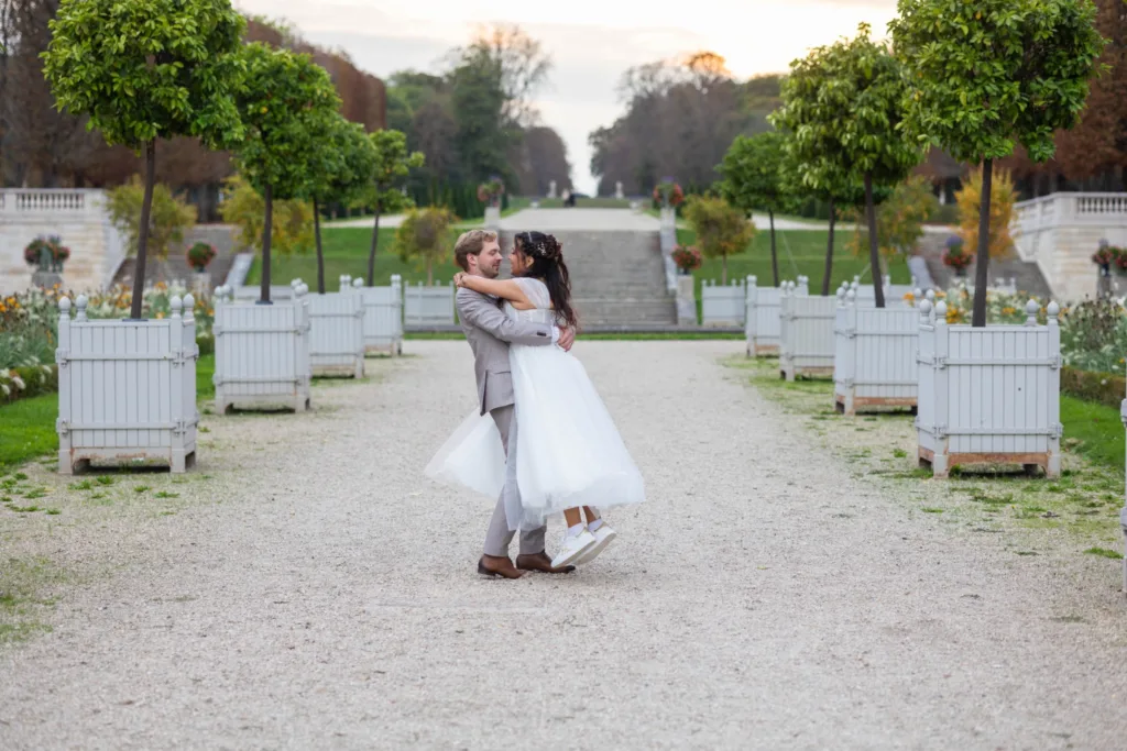 Le marié fait tourner la mariée dans une allée bordée de caisses de Versailles, parc de Saint-Cloud