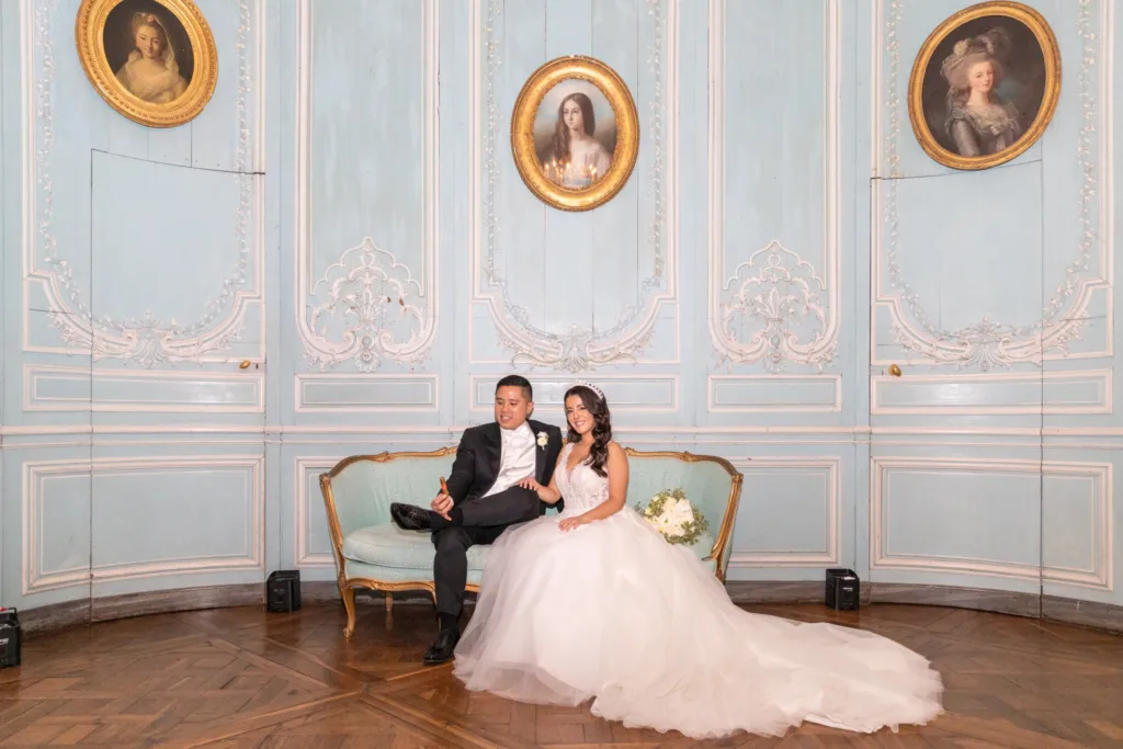 Mariés assis sur la banquette du salon bleu aux boiseries rocaille du Château de Champlâtreux
