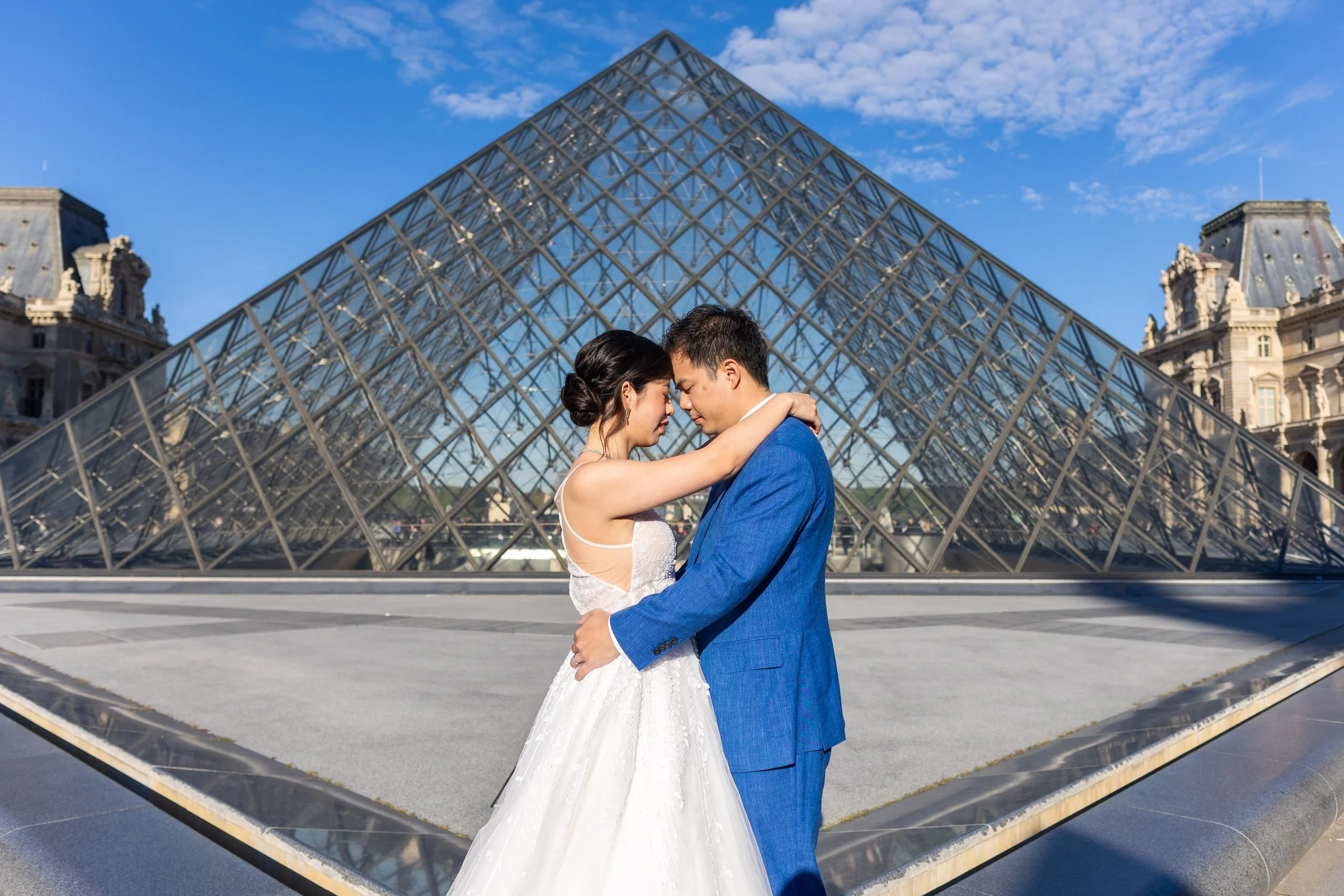 Mariés enlacés front contre front devant la pyramide du Louvre