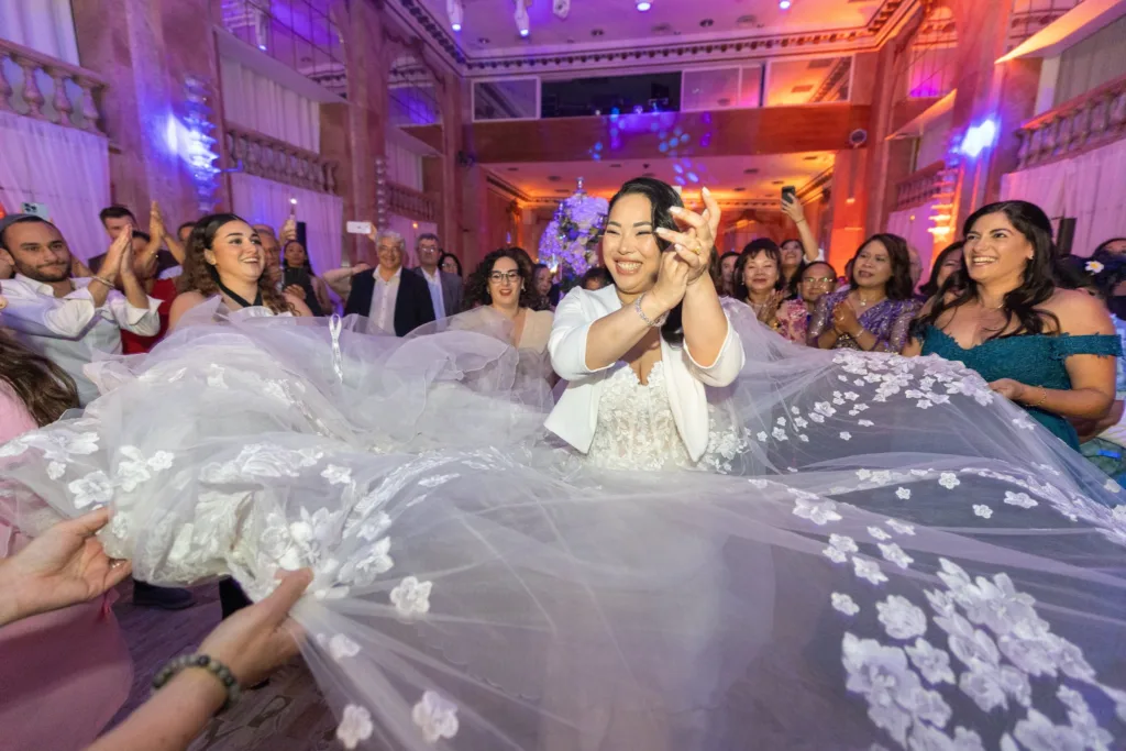 Monita radieuse pendant que les invités tiennent son voile brodé de fleurs lors de la réception
