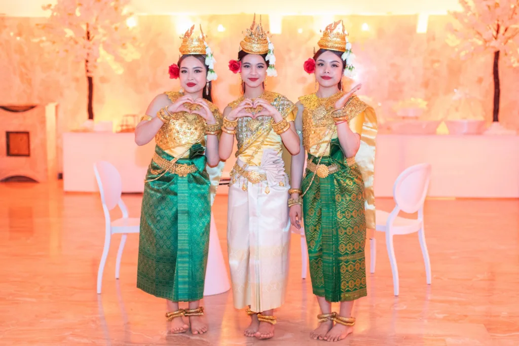 Trois danseuses cambodgiennes en costumes traditionnels dorés et verts formant un cœur avec leurs mains