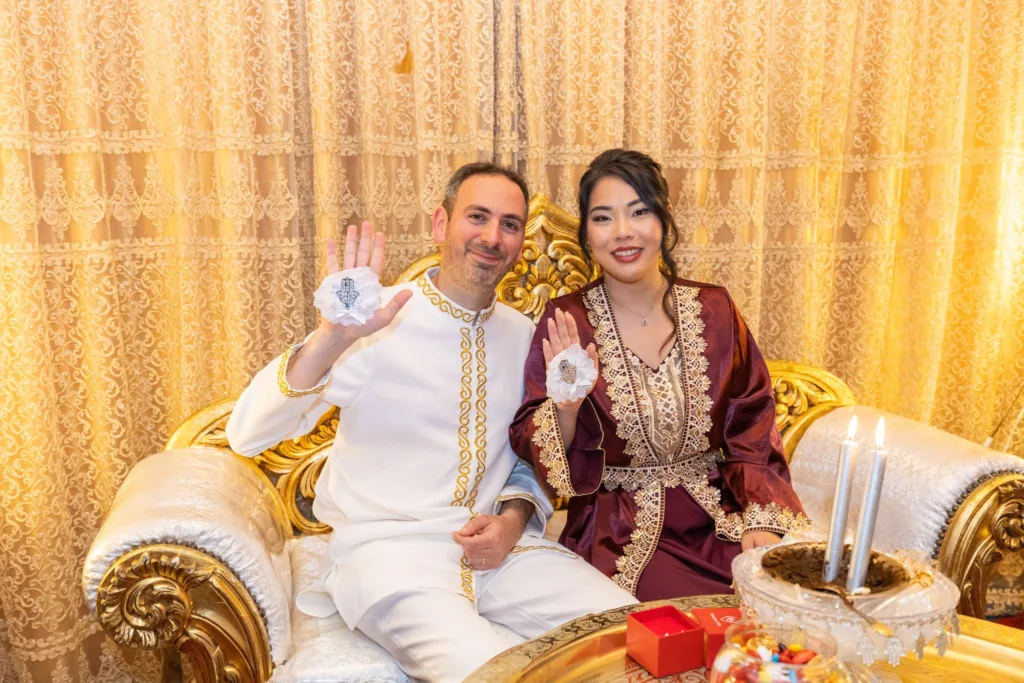 Monita et Jérémy en caftans brodés d'or lors de la soirée du henné, mains levées ornées de la khamsa