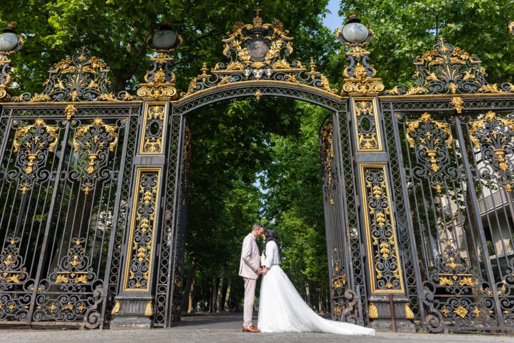Les mariés s'embrassant sous une grande grille dorée d'un parc parisien, Monita en robe de mariée à traîne