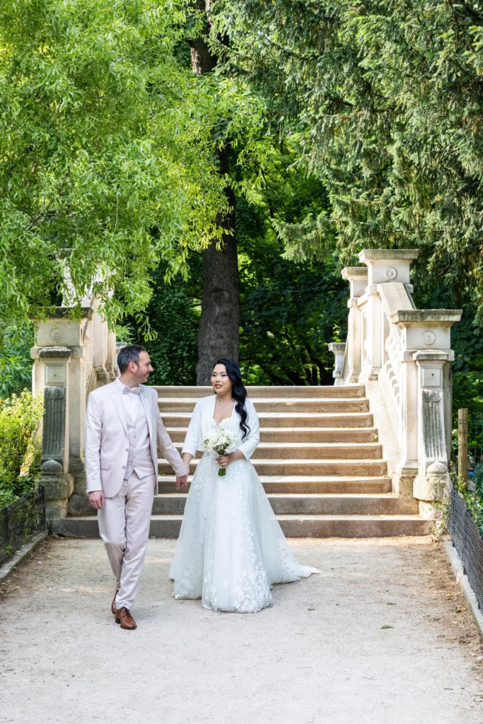 Monita et Jérémy main dans la main au pied d'un escalier en pierre dans un parc parisien